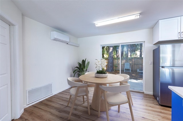 dining area with light wood finished floors, visible vents, an AC wall unit, and baseboards