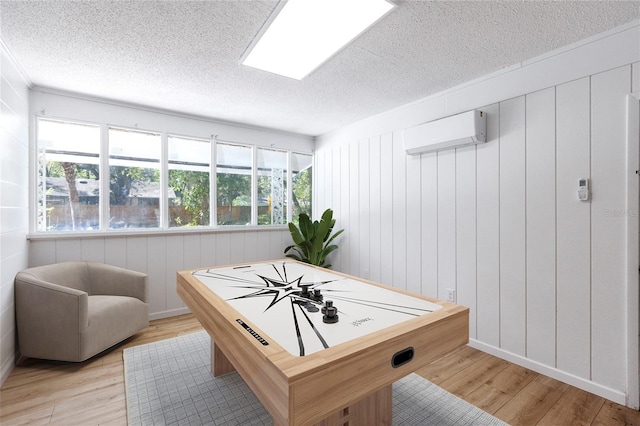 game room with a textured ceiling, a skylight, light wood-type flooring, and a wall unit AC