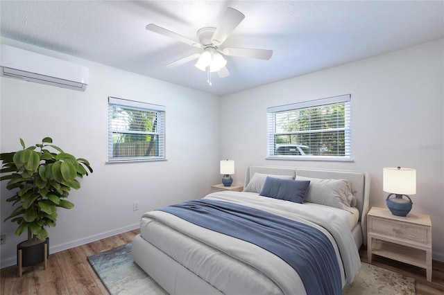 bedroom with wood finished floors, baseboards, ceiling fan, an AC wall unit, and a textured ceiling