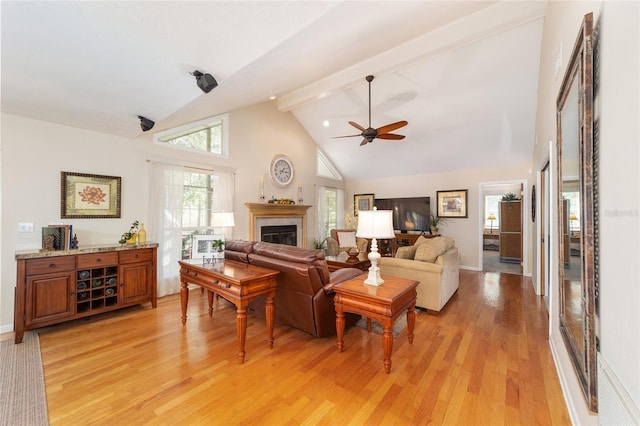 living room featuring a ceiling fan, high vaulted ceiling, light wood-style floors, a glass covered fireplace, and beamed ceiling