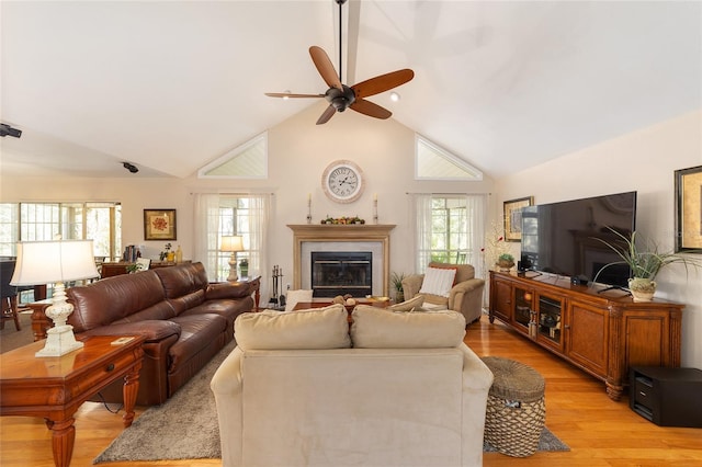 living room featuring a glass covered fireplace, high vaulted ceiling, light wood-type flooring, and a ceiling fan