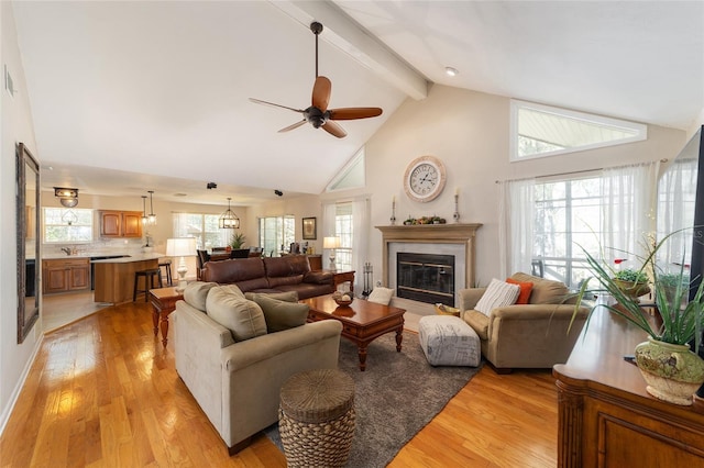 living area featuring a glass covered fireplace, beam ceiling, light wood finished floors, and high vaulted ceiling