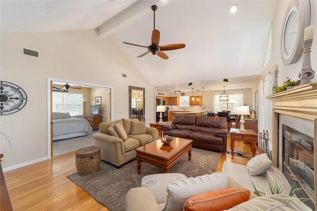 living area featuring a wealth of natural light, visible vents, beamed ceiling, and light wood-style flooring