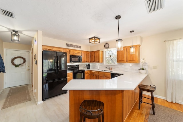 kitchen featuring visible vents, a peninsula, a sink, black appliances, and tasteful backsplash