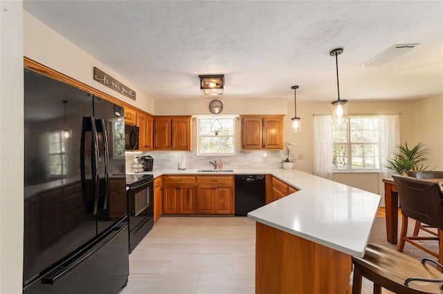 kitchen featuring black appliances, a sink, a peninsula, brown cabinetry, and light countertops