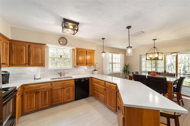 kitchen with a breakfast bar area, a peninsula, a sink, black appliances, and light countertops