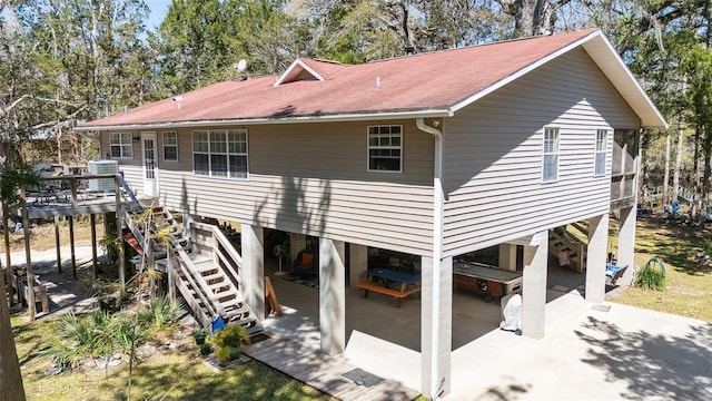 back of property with stairway, a patio area, and roof with shingles