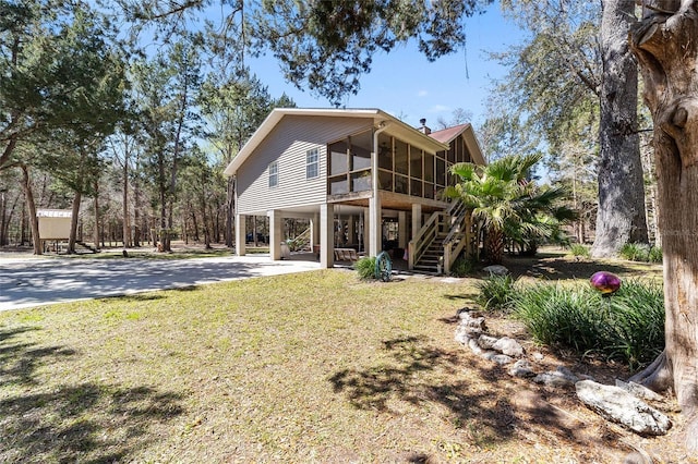 rear view of property featuring stairway, a yard, a sunroom, concrete driveway, and a carport