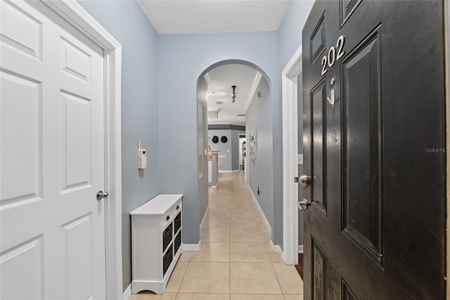 hallway with light tile patterned floors, baseboards, arched walkways, and a textured ceiling