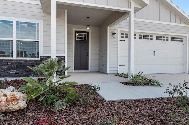 doorway to property featuring stone siding, board and batten siding, an attached garage, and concrete driveway