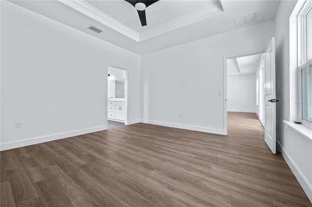 spare room featuring a tray ceiling, wood finished floors, visible vents, and baseboards