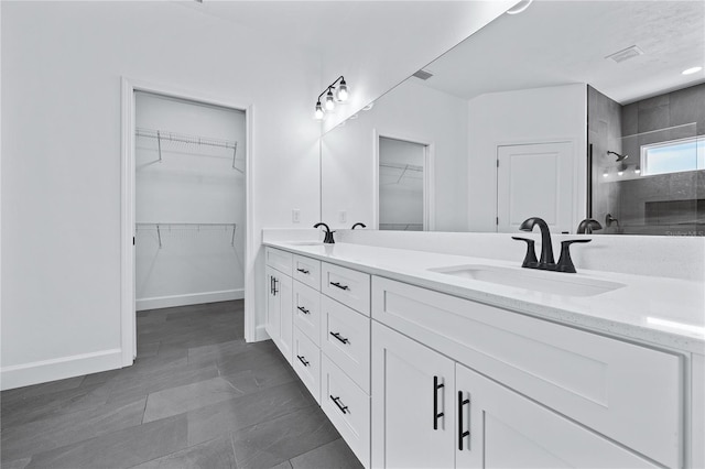 bathroom featuring visible vents, baseboards, double vanity, tiled shower, and a sink