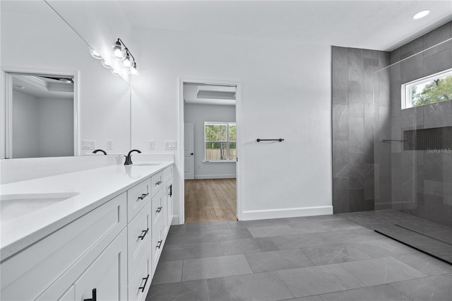 full bath featuring double vanity, a walk in shower, baseboards, and a sink