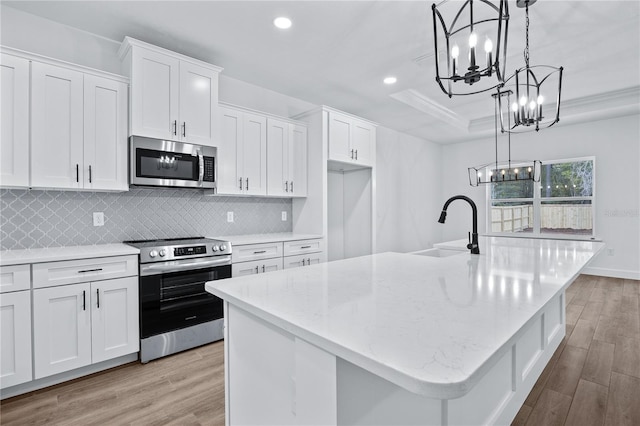 kitchen featuring a sink, a tray ceiling, light wood-type flooring, and appliances with stainless steel finishes