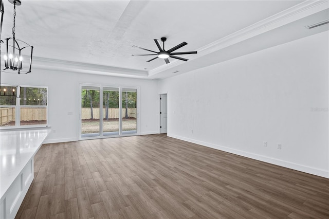 unfurnished living room featuring crown molding, baseboards, dark wood-type flooring, a tray ceiling, and ceiling fan with notable chandelier