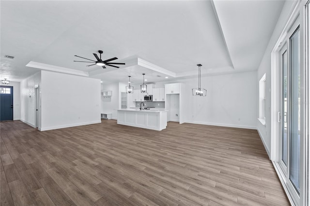 unfurnished living room with visible vents, ceiling fan with notable chandelier, a sink, a tray ceiling, and wood finished floors