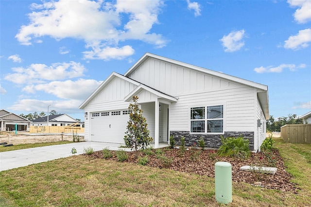 view of front of house featuring an attached garage, board and batten siding, fence, stone siding, and driveway