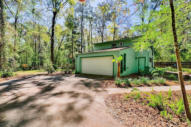 garage featuring a wooded view, driveway, and fence