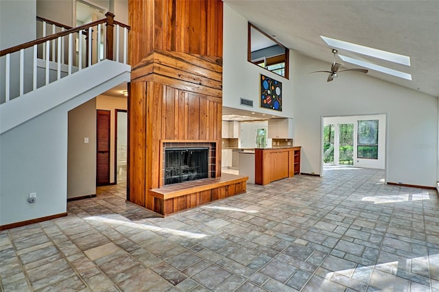 unfurnished living room featuring baseboards, visible vents, a skylight, a tile fireplace, and ceiling fan