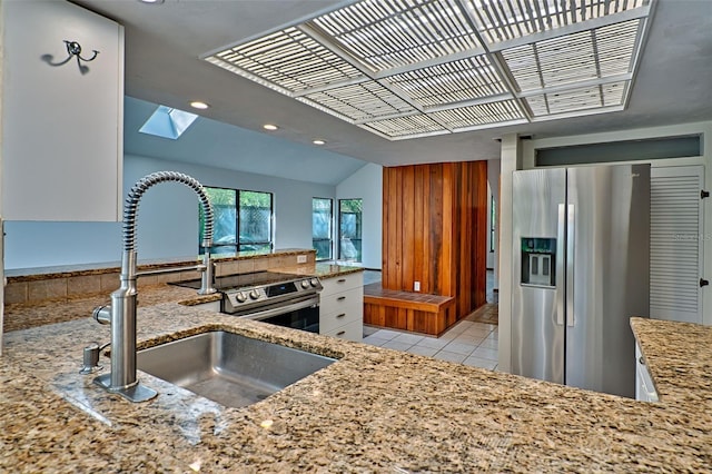 kitchen featuring a sink, vaulted ceiling with skylight, light tile patterned flooring, stainless steel fridge with ice dispenser, and light stone countertops