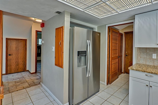 kitchen with visible vents, light stone countertops, stainless steel fridge with ice dispenser, decorative backsplash, and white cabinets