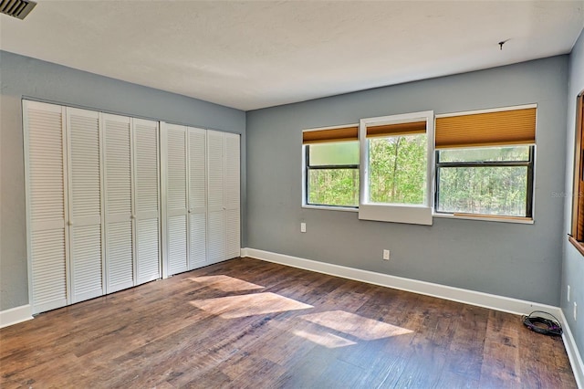 unfurnished bedroom with a closet, visible vents, baseboards, and wood finished floors