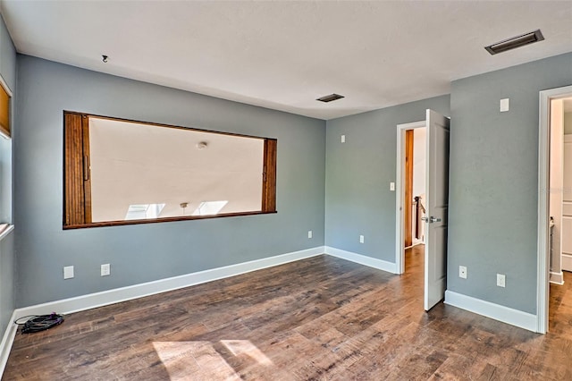 spare room with wood finished floors, visible vents, and baseboards