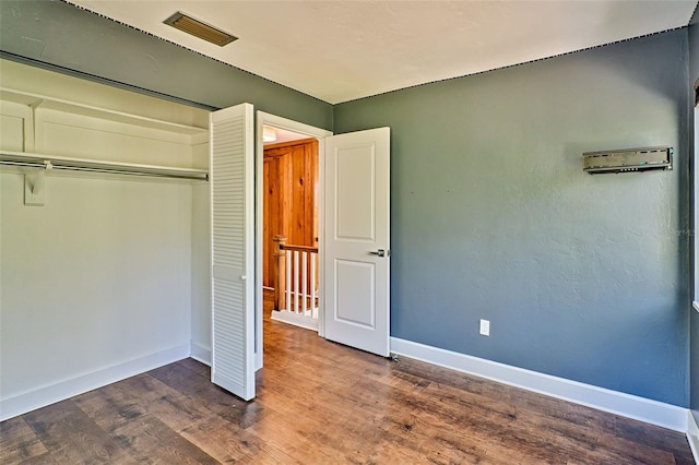 unfurnished bedroom featuring dark wood-type flooring, baseboards, visible vents, and a closet