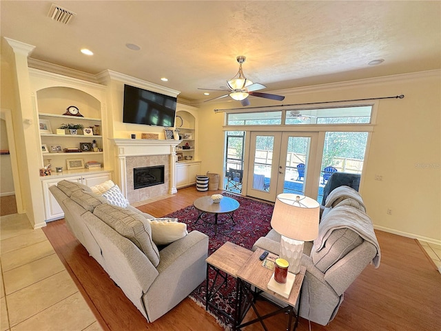 living area with visible vents, built in shelves, ceiling fan, a fireplace, and french doors