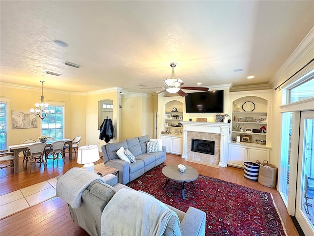 living room featuring visible vents, light wood-style flooring, ceiling fan with notable chandelier, built in features, and crown molding