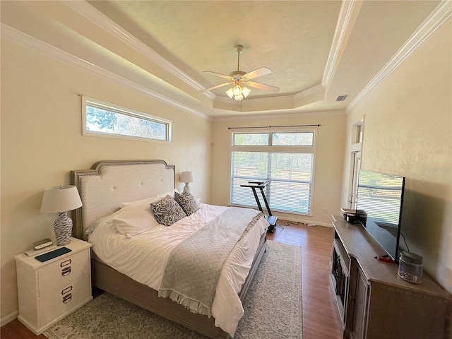 bedroom featuring a tray ceiling, multiple windows, wood finished floors, and crown molding