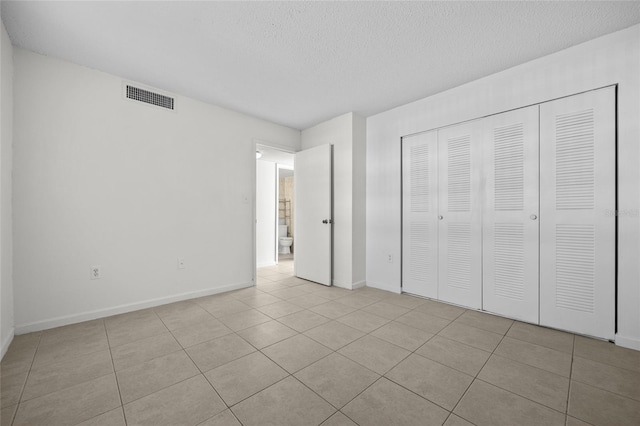 unfurnished bedroom with visible vents, a textured ceiling, a closet, tile patterned flooring, and baseboards