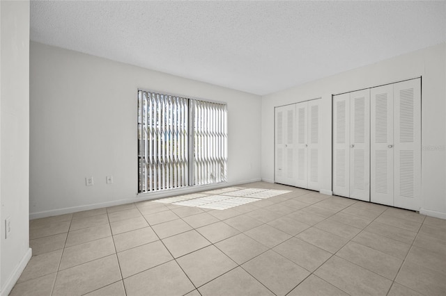 unfurnished bedroom featuring light tile patterned floors, baseboards, two closets, and a textured ceiling