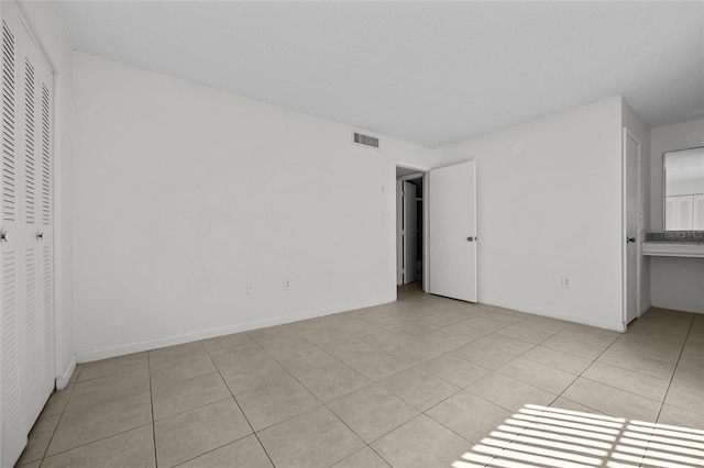 unfurnished bedroom featuring light tile patterned flooring, visible vents, a closet, and baseboards