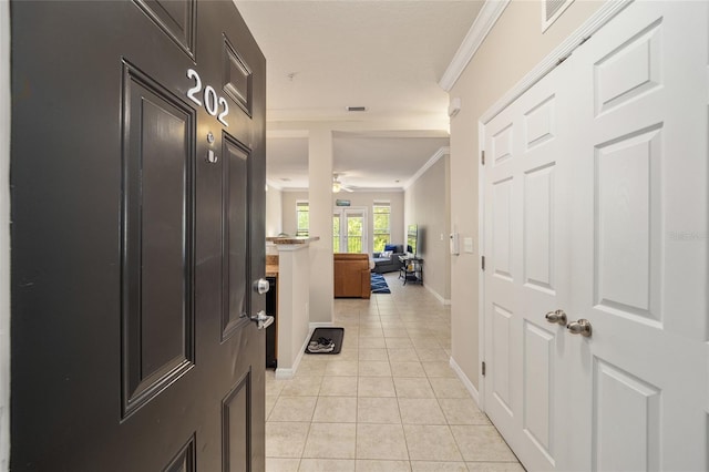 hall featuring light tile patterned floors, baseboards, and crown molding