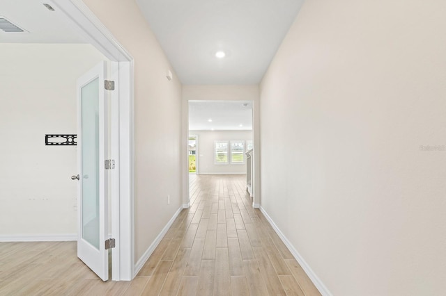 hall with light wood-style floors, visible vents, and baseboards