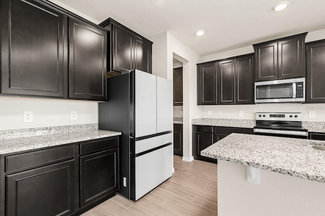 kitchen with light stone countertops, wood tiled floor, recessed lighting, appliances with stainless steel finishes, and dark cabinetry