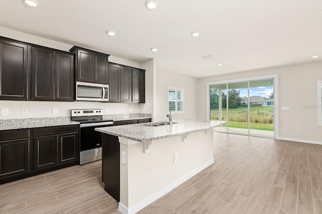 kitchen with light stone counters, a center island with sink, wood tiled floor, a sink, and appliances with stainless steel finishes