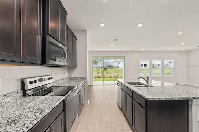 kitchen with visible vents, a sink, light stone countertops, appliances with stainless steel finishes, and a kitchen island with sink