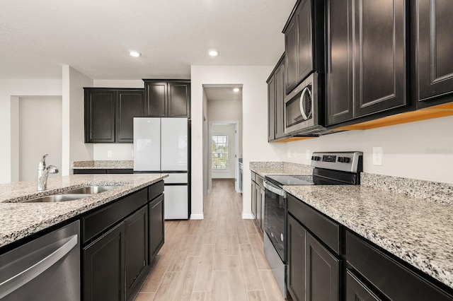 kitchen featuring light stone countertops, recessed lighting, light wood-style flooring, stainless steel appliances, and a sink