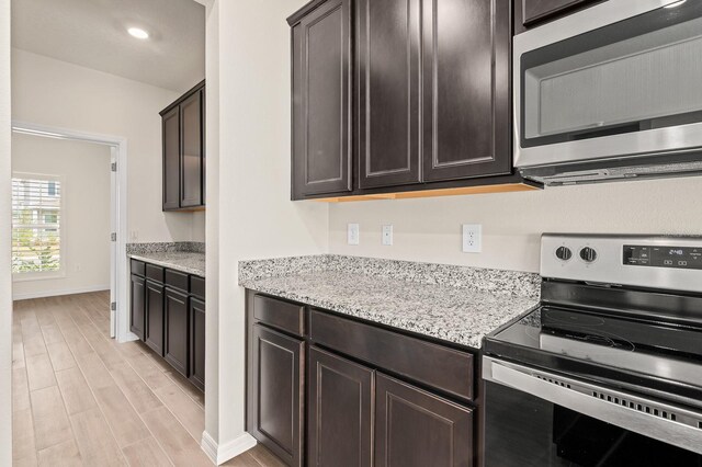 kitchen with light wood finished floors, dark brown cabinets, baseboards, light stone countertops, and appliances with stainless steel finishes