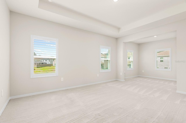 empty room featuring recessed lighting, baseboards, a raised ceiling, and light colored carpet