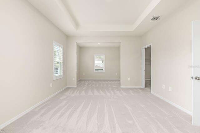 unfurnished room featuring a tray ceiling, baseboards, visible vents, and light carpet