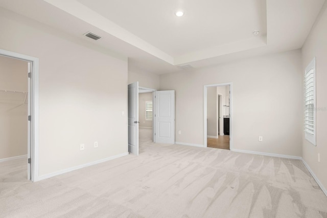 unfurnished bedroom with visible vents, a raised ceiling, light carpet, and a spacious closet