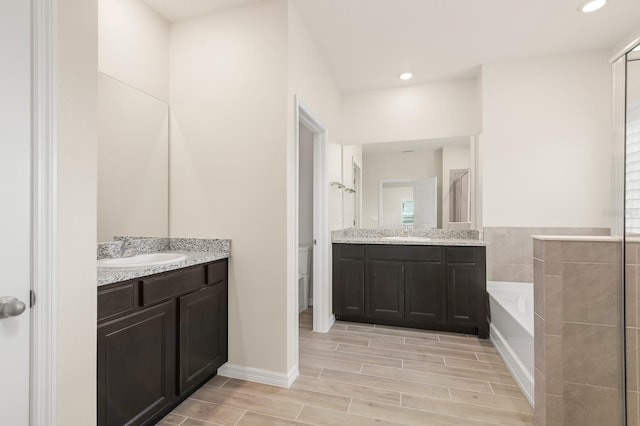 bathroom featuring wood finish floors, two vanities, recessed lighting, a sink, and a garden tub