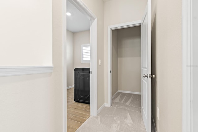 corridor with light wood finished floors, washer / clothes dryer, and baseboards