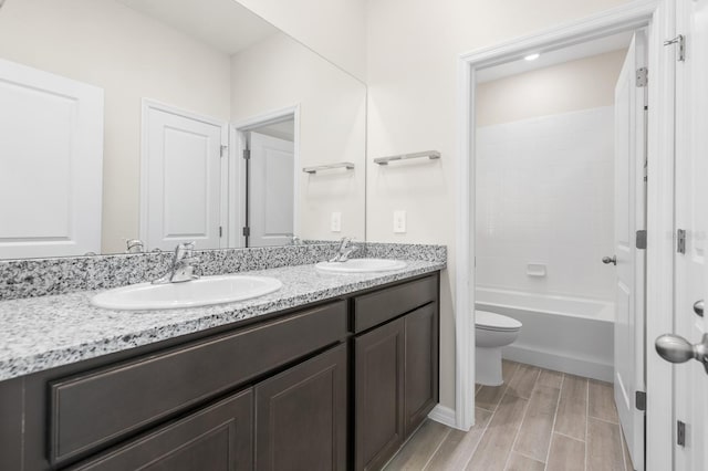 bathroom with a sink, wood tiled floor, double vanity, and toilet