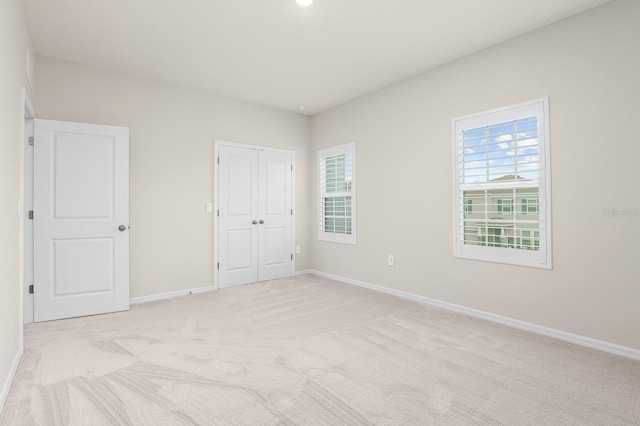 unfurnished bedroom with multiple windows, light carpet, baseboards, and a closet