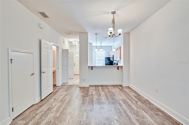 unfurnished dining area with a chandelier, visible vents, light wood-style flooring, and baseboards