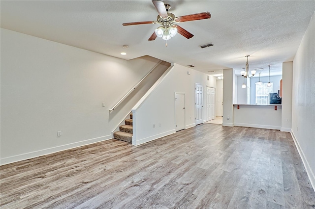 unfurnished living room with visible vents, stairs, ceiling fan with notable chandelier, wood finished floors, and a textured ceiling